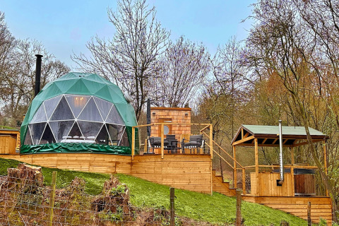 Ashdown Luxury Dome featuring a glamping geodome, wooden deck, outdoor seating, and forest backdrop.