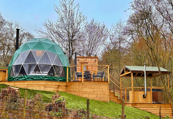 Ashdown Luxury Dome featuring a glamping geodome, wooden deck, outdoor seating, and forest backdrop.
