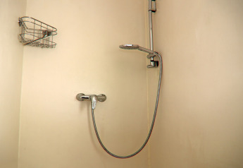 Ducha moderna en un cuarto de baño de casa flotante, con cabezal ajustable y estante metálico para artículos.