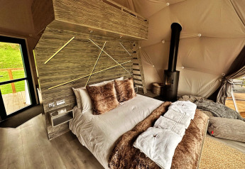 Interieur van de Wakehurst Luxury Dome in het VK met comfortabel bed, haard en moderne details.