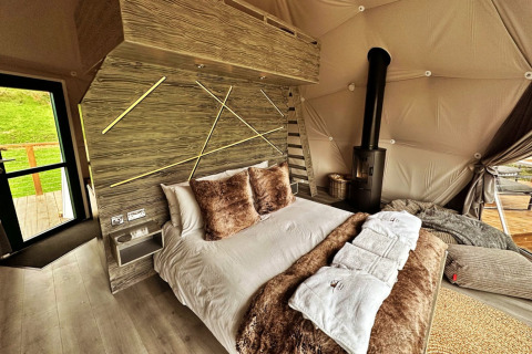 Wakehurst Luxury Dome interior in the UK, featuring a comfy bed, cozy decor, fireplace, and modern accents.