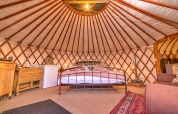 Gemütliches Inneres einer Bramble Yurt im Vereinigten Königreich mit Bett, Teppich und Möbeln.