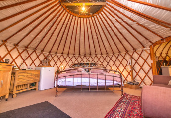 Gemütliches Inneres einer Bramble Yurt im Vereinigten Königreich mit Bett, Teppich und Möbeln.