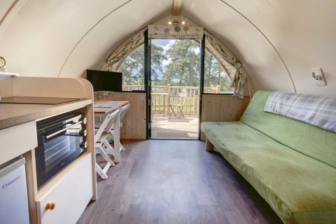 Knus pod-interieur met groene bank, kitchenette, opklaptafel en glazen deuren naar het terras buiten.