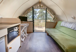 Knus pod-interieur met groene bank, kitchenette, opklaptafel en glazen deuren naar het terras buiten.