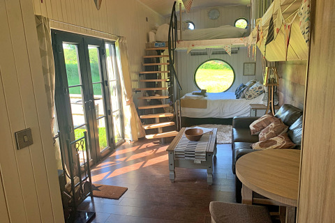 Intérieur du mobil-home Oak Tree Lodge au Royaume-Uni avec canapé, escalier en colimaçon et grandes fenêtres.