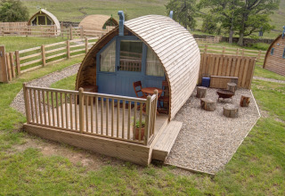 Foto van een gezellige houten pod met veranda, buitenterras en vuurplaats in een groene landelijke omgeving.