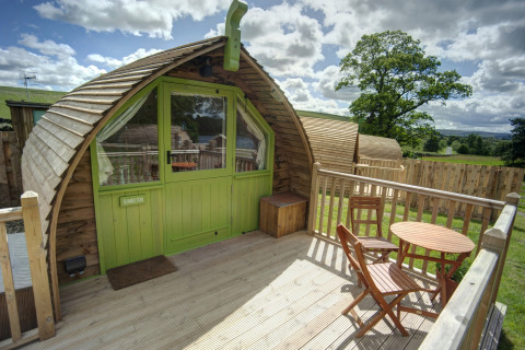 Houten terras voor Humbleton Glamping pod met tafel en stoelen, omgeven door natuur en omheining.
