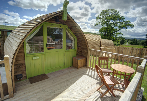Houten terras voor Humbleton Glamping pod met tafel en stoelen, omgeven door natuur en omheining.