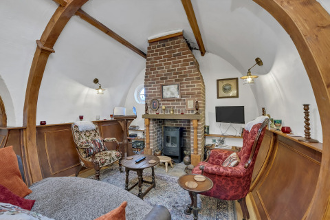 Spazio living accogliente nel Pod 'Hollow', UK, con camino in mattoni, archi in legno e arredi d’epoca.