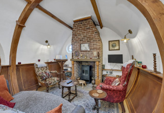 Spazio living accogliente nel Pod 'Hollow', UK, con camino in mattoni, archi in legno e arredi d’epoca.