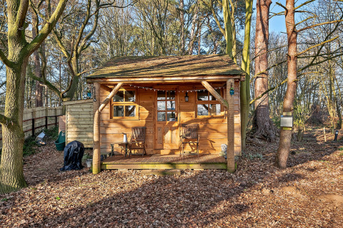 Træchalet kaldet Cedar Lodge, omgivet af træer i en skovklædt natur, med veranda og træstole foran.