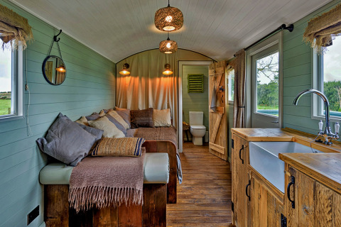 Gezellig interieur van de 'Joan' Shepherds Hut mobiele woning in het VK met houten meubels en sofa.