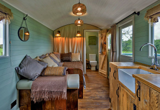 Gezellig interieur van de 'Joan' Shepherds Hut mobiele woning in het VK met houten meubels en sofa.