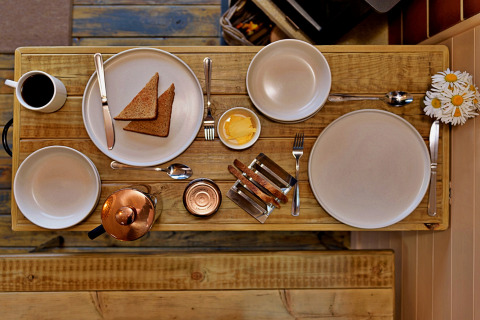 Tiny wooden breakfast table with toast, butter, coffee and flowers at 'Marared' Gypsy Hut, United Kingdom.