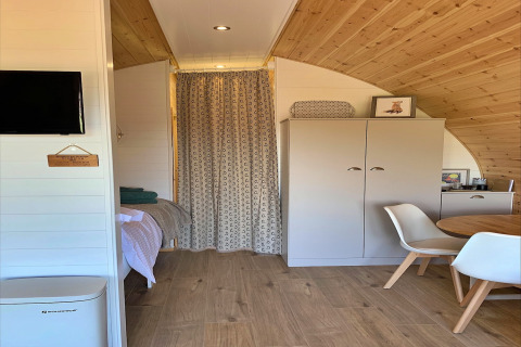 Intérieur du pod Worm Dale au Royaume-Uni avec plafond en bois, lit, armoire et table à manger.
