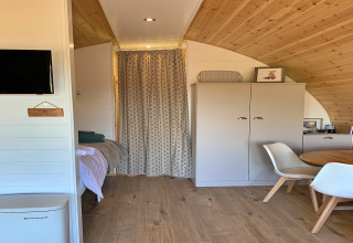 Intérieur du pod Worm Dale au Royaume-Uni avec plafond en bois, lit, armoire et table à manger.