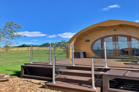 Modern wooden pod named 'Deep Dale' in the UK, with glass railing, deck, and scenic landscape.
