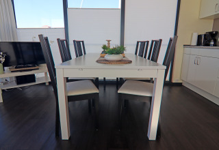 Eettafel met acht stoelen op een moderne woonboot, licht interieur, grote ramen, donkere vloer.