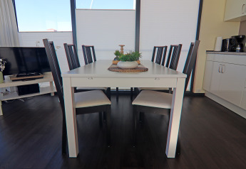 Eettafel met acht stoelen op een moderne woonboot, licht interieur, grote ramen, donkere vloer.