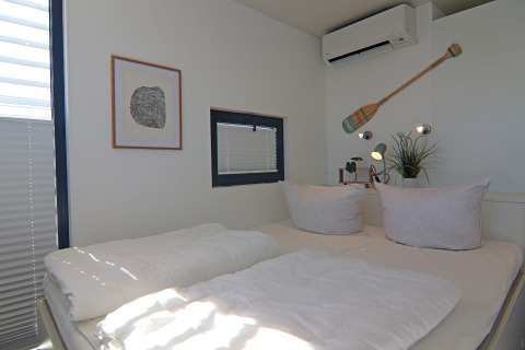 Modern ingerichte slaapkamer op een woonboot met airconditioning, planten en minimalistische decoratie.