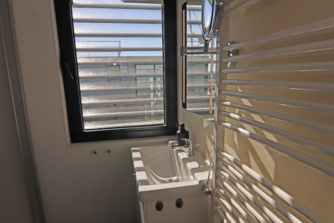 Kleine badkamer op de woonboot Family & Friends LP 3 met lavabo, raam en witte handdoekradiator aan de muur.