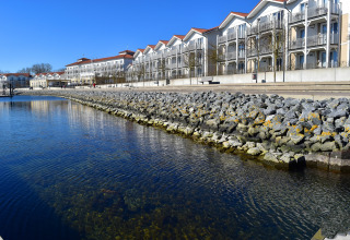 Vista desde la casa flotante Family & Friends LP 3 al agua tranquila y apartamentos modernos en Alemania.