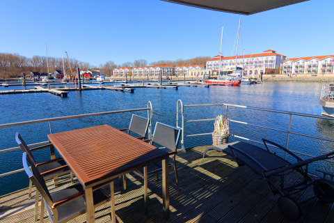 View from houseboat terrace with table and chairs overlooking marina, boats, and apartments in Germany.