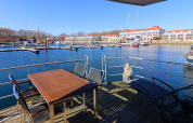 Blick von einer Hausboot-Terrasse mit Tisch und Stühlen auf einen Jachthafen mit Segelbooten in Deutschland.