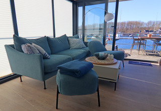 Bright living area on a houseboat with a blue sofa, water views, and an outdoor dining space by the marina.