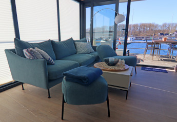 Salon lumineux sur une péniche avec canapé bleu, vue sur l'eau et coin repas extérieur près du port.