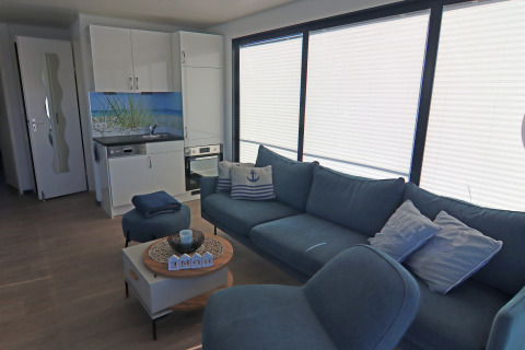 Modern living room and kitchenette on Houseboat Family & Friends LP 4 with blue sofa and large windows.