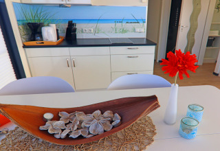 Modernes Hausboot-Küche mit Holzdeko, roter Blume in Vase und blauen Teelichtern auf dem Tisch.