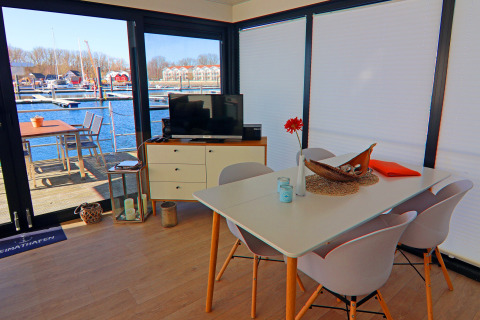 Modern dining and TV area on a houseboat with marina view through large windows in Germany.