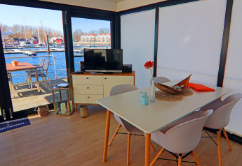 Modern dining and TV area on a houseboat with marina view through large windows in Germany.