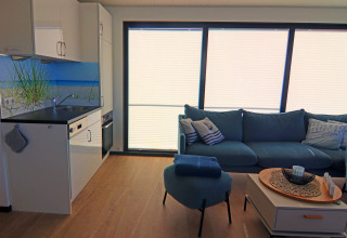 Modern houseboat interior with sleek kitchen, blue sofa, large windows and maritime decor in Germany.