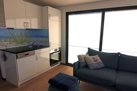 Modern living area and kitchenette on a houseboat with large windows, blue sofa and nautical cushions.