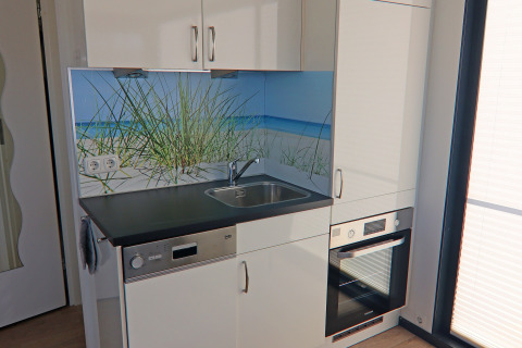 Modern kitchenette on a houseboat with sink, oven and beach mural backsplash, located in Germany.