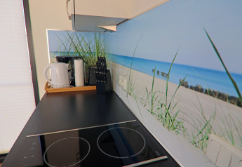 Moderne Küchenarbeitsplatte mit schwarzem Kochfeld, Wasserkocher und Strandmotiv in Hausboot Deutschland.