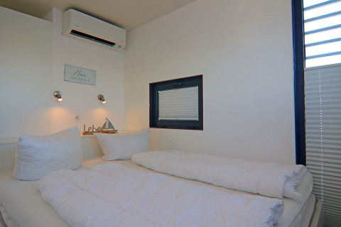 Dormitorio con cama doble, almohadas blancas, iluminación moderna y ventana en una casa flotante en Alemania.