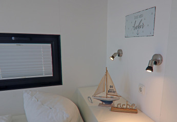 Schlafzimmer auf einem Hausboot mit Modellsegelboot, Wandlampen und Schild 'Du bist mein Anker' in Deutschland.