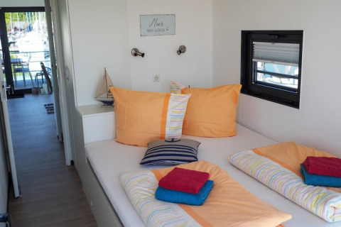 Houseboat bedroom with colorful bedding, nautical-themed decor, and a view of a marina through the window.
