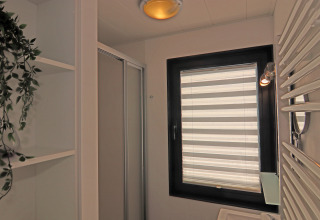 Bathroom on a houseboat in Germany with window blinds, shower cabin, shelving, and greenery.