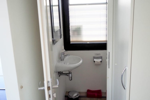 A small houseboat bathroom featuring a wall-mounted sink, mirror, toilet paper holder and frosted window.