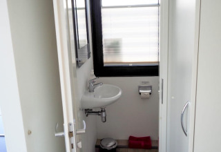 Un pequeño baño en una casa flotante con lavabo de pared, espejo, portarrollo y ventana esmerilada.