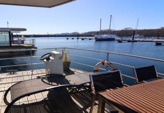 Solrig udsigt fra husbåd Family & Friends LP 4, med havemøbler og styrhjul ved en tysk marina.