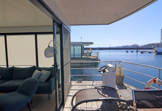 View from a houseboat in Germany with a terrace, helm, lounge chair, and sofa in the living area.