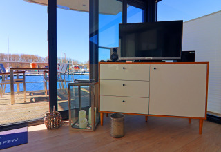 Living area in a houseboat with TV on a sideboard, candles, and view of deck overlooking harbor and boats.