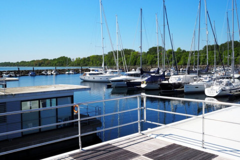 View from a houseboat overlooking a marina filled with sailboats, calm water, and lush green trees.