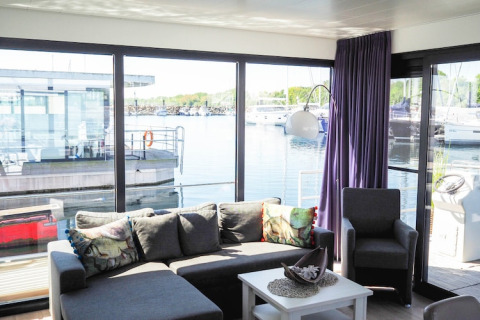 Bright, modern living room on a houseboat with large windows and marina views in Germany.
